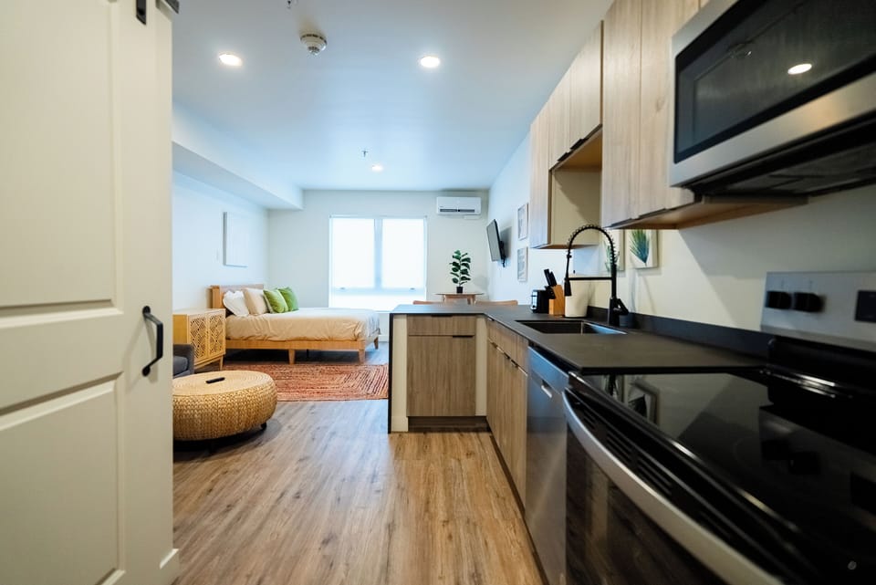 Step into your stylish studio where modern kitchen meets cozy bedroom, featuring warm wood tones and thoughtful design for comfortable extended stays.