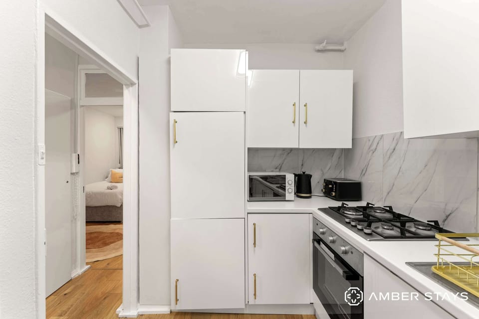 This compact, modern kitchen features sleek all-white cabinetry accented by gold hardware and a grey-veined marble backsplash.