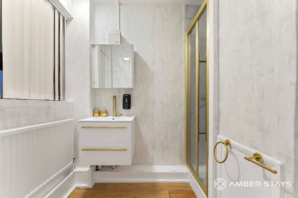 A white floating vanity and gold-trimmed shower create a sleek, modern look against textured walls. Brushed gold hardware throughout adds a luxurious touch to this minimalist bathroom.