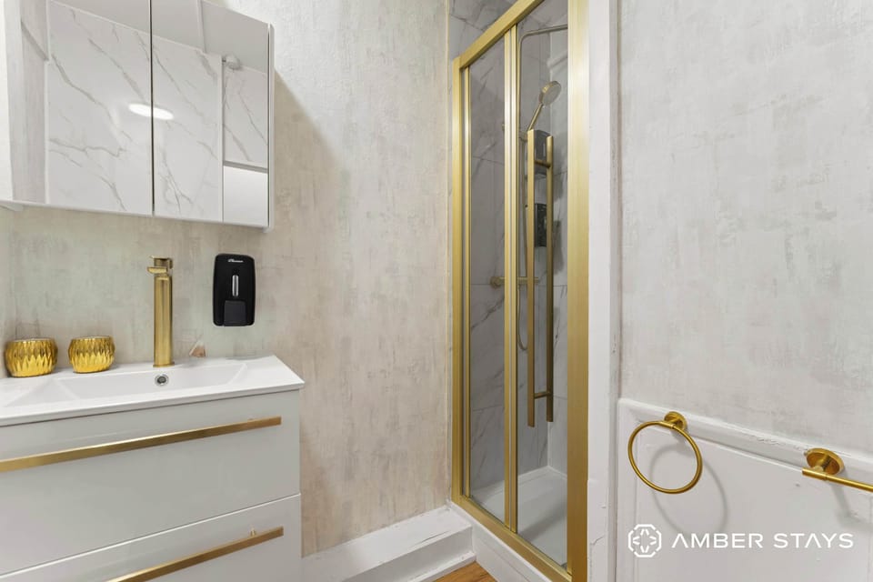 A white floating vanity and gold-trimmed shower create a sleek, modern look against textured walls. Brushed gold hardware throughout adds a luxurious touch to this minimalist bathroom.