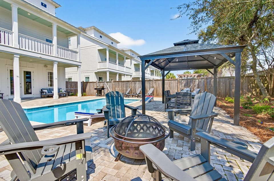 Resort-style backyard oasis in Miramar Beach with a private heated pool, covered gazebo dining, outdoor kitchen, fire pit with lounge seating, cornhole, and a covered porch for relaxing in the shade. Perfect for unforgettable vacations!