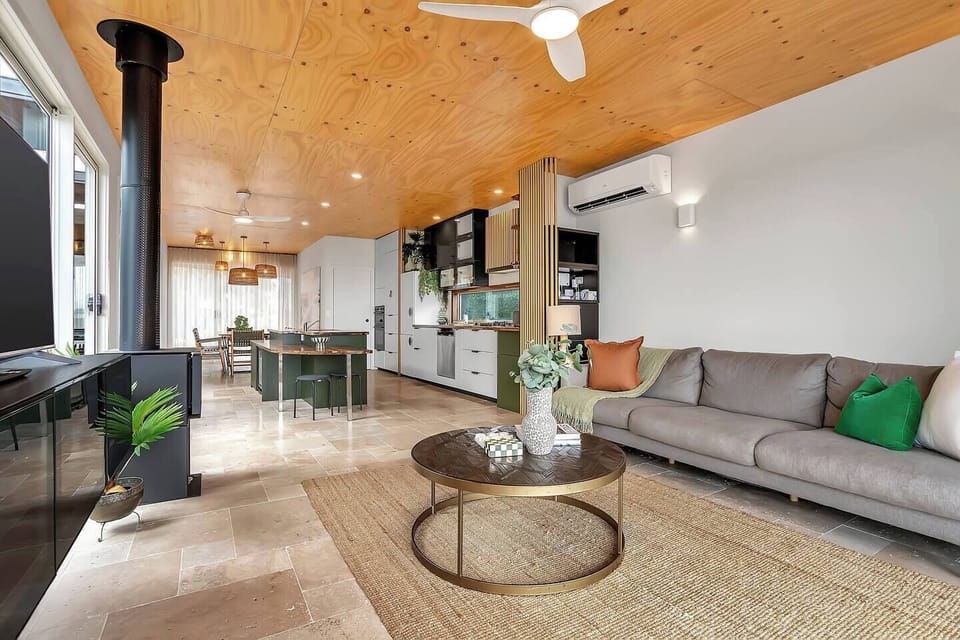 The living room is a warm, light-filled sanctuary, anchored by the fireplace and framed by expansive glass capturing uninterrupted water views.