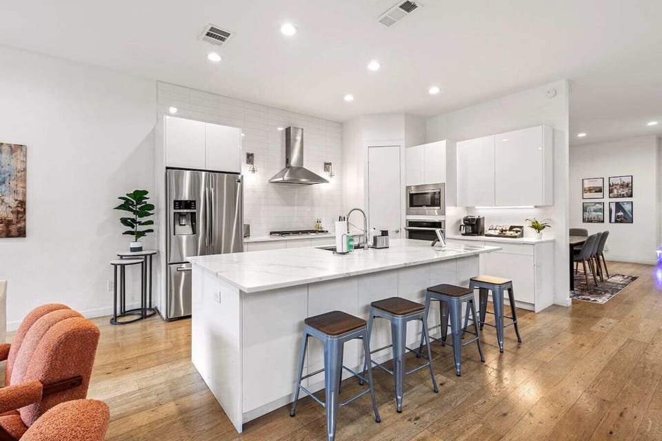 Modern chef’s kitchen featuring a spacious island, stainless steel appliances, and sleek white cabinetry — perfect for cooking and gathering.