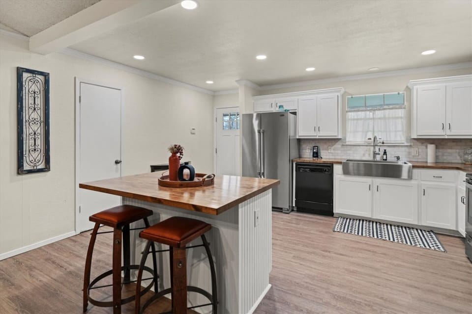 Full kitchen view featuring white shaker cabinets, a butcher block island with bar seating, French door refrigerator, farmhouse sink, and full suite of appliances — a generously sized and beautifully appointed space ready for serious home cooking.