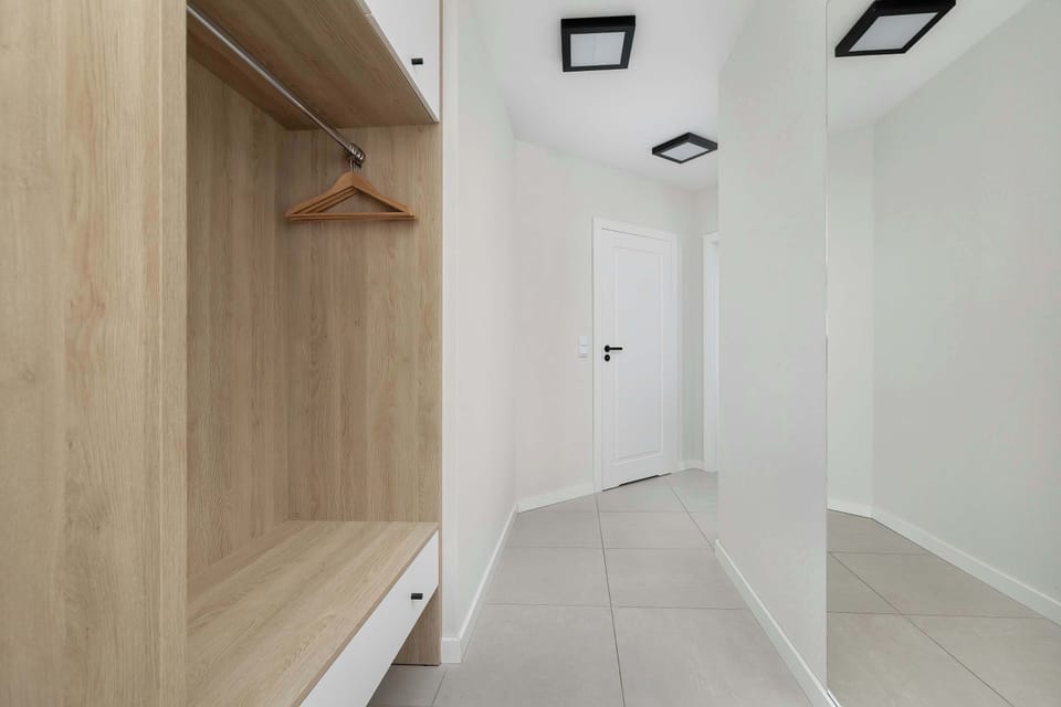 A built-in wooden wardrobe offers plenty of space for coats and luggage right by the entrance. The light-colored flooring and white walls maintain the apartment's airy and modern feel.
