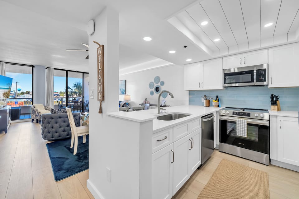 Your modern kitchen flows seamlessly into the bright living space, where crisp white cabinetry and stainless steel appliances provide ample space for preparing meals.