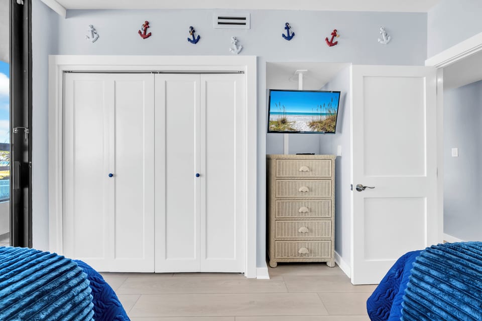 Unpack and settle into your nautical-themed bedroom with ample closet space, wicker storage, and coastal TV entertainment beneath cheerful anchor decor.