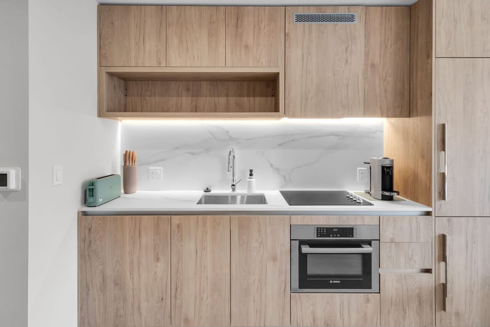 Modern kitchenette featuring sleek wood cabinetry, marble backsplash, and premium appliances. Equipped with a stovetop, oven, and Nespresso machine, it’s perfect for preparing quick meals or your morning coffee.