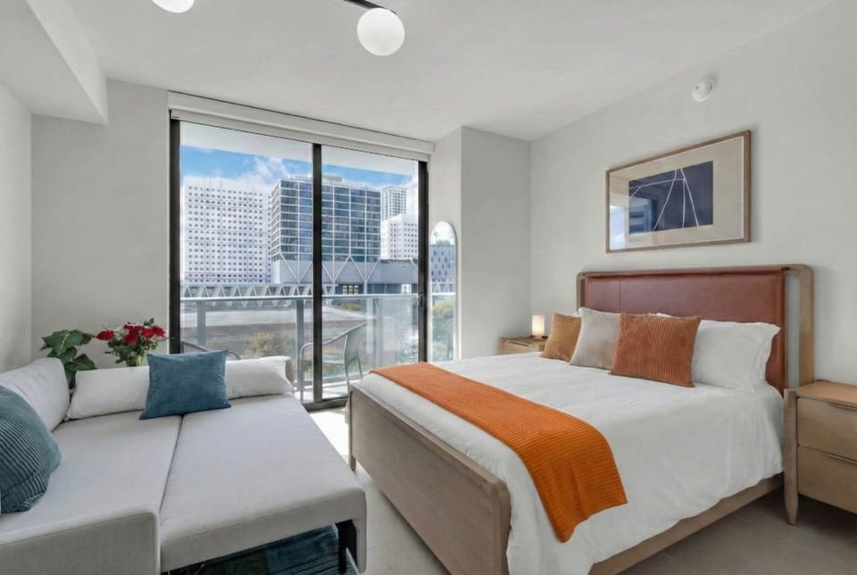 Relax in this sun-drenched studio featuring a plush queen bed, a versatile sofa lounge, and a private balcony with stunning city views. Modern decor and floor-to-ceiling windows create the perfect urban retreat.