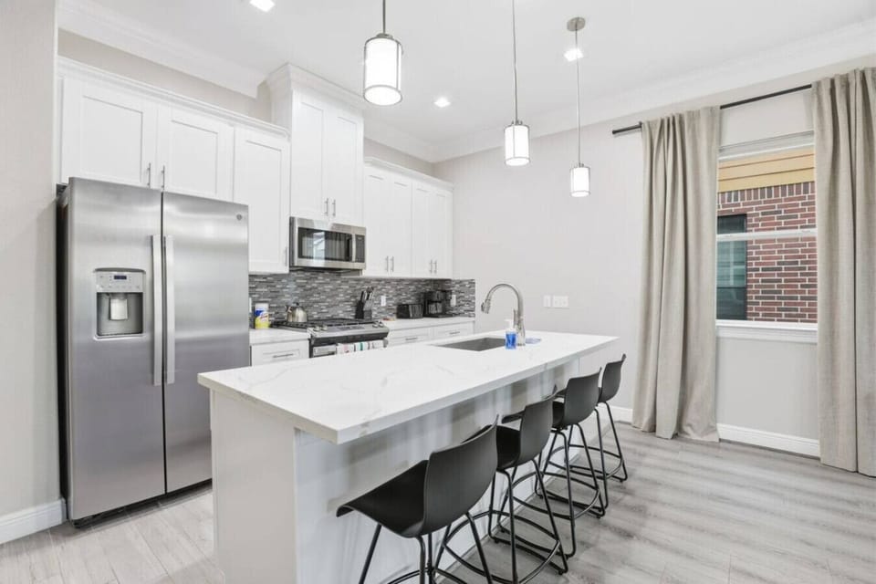 A sleek kitchen setup with generous counter seating, modern finishes, and bright lighting—ideal for casual meals or gathering while cooking.