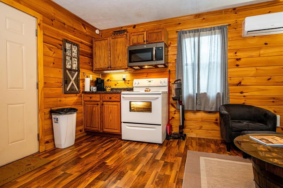 Compact kitchen corner with oak cabinets, white electric stove, black coffee maker, and warm wood plank floors.