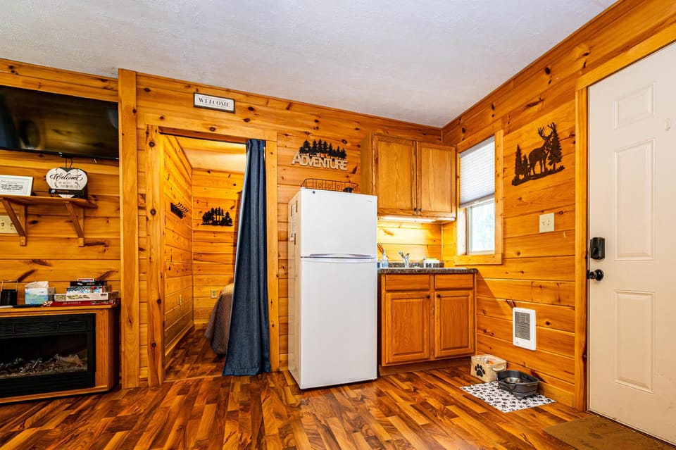 Compact kitchenette with oak cabinets, granite countertop, white refrigerator, and wood-paneled walls and ceiling.