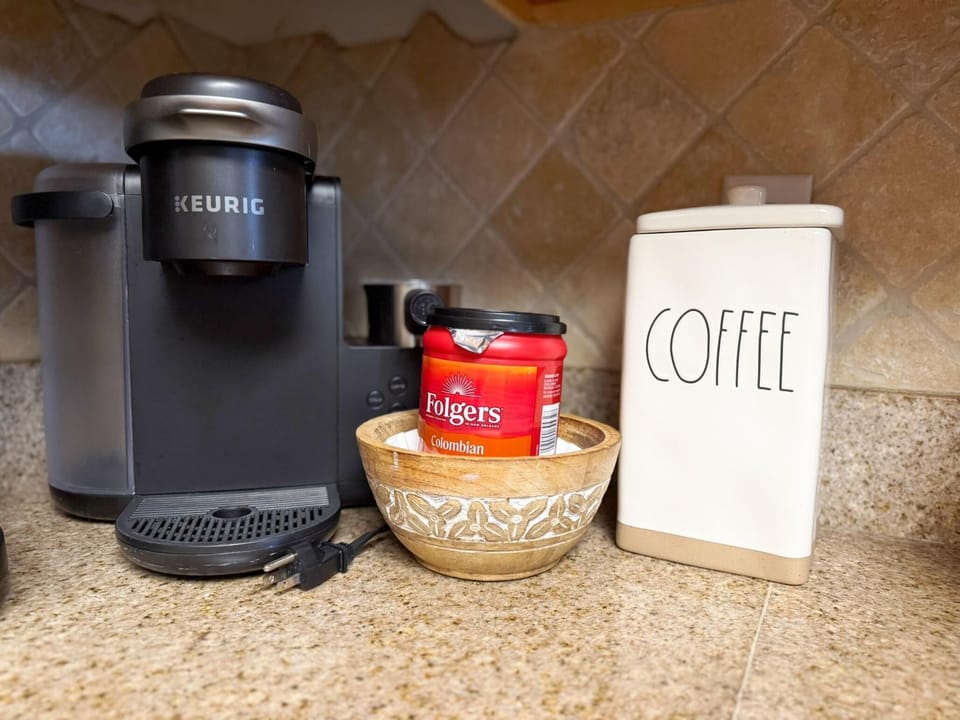 Black Keurig coffee maker sits on granite countertop beside a wooden bowl and white ceramic coffee canister.