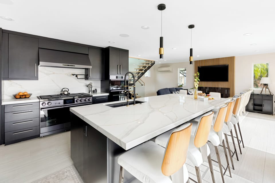 Kitchen featuring sleek black cabinetry paired with white marble countertops and gold-toned stools.