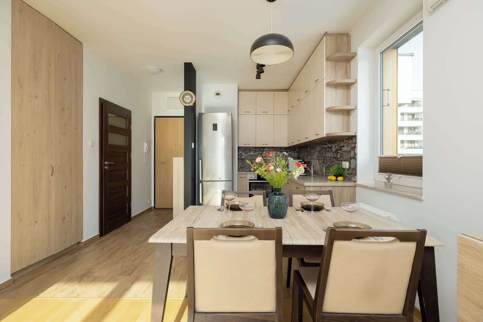 The kitchenette and dining zone are seamlessly integrated, featuring modern light-wood cabinetry and a tall silver refrigerator and a sleek wooden dining table set for four.