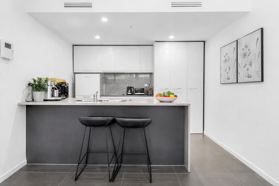 Modern white kitchen with breakfast bar, full fridge, and coffee setup.