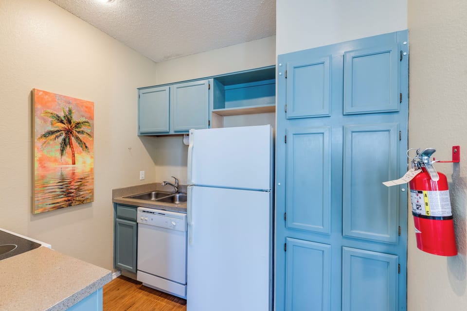 Your fully equipped kitchenette features charming blue cabinets, modern appliances, and cheerful tropical artwork to brighten your cooking adventures.