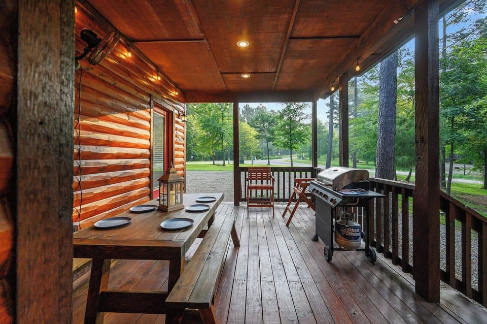 Your covered porch awaits with dining table set for outdoor meals and BBQ grill ready for cookouts overlooking peaceful woods.