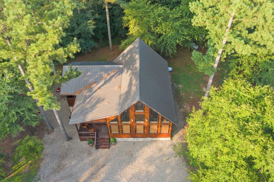 Modern cabin nestled in lush forest with expansive glass windows and metal roofing, surrounded by towering trees and natural beauty.