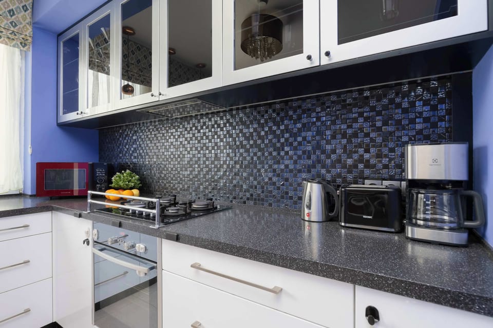A modern kitchen with white cabinetry and a black tiled backsplash. Small appliances sit neatly on the countertop.