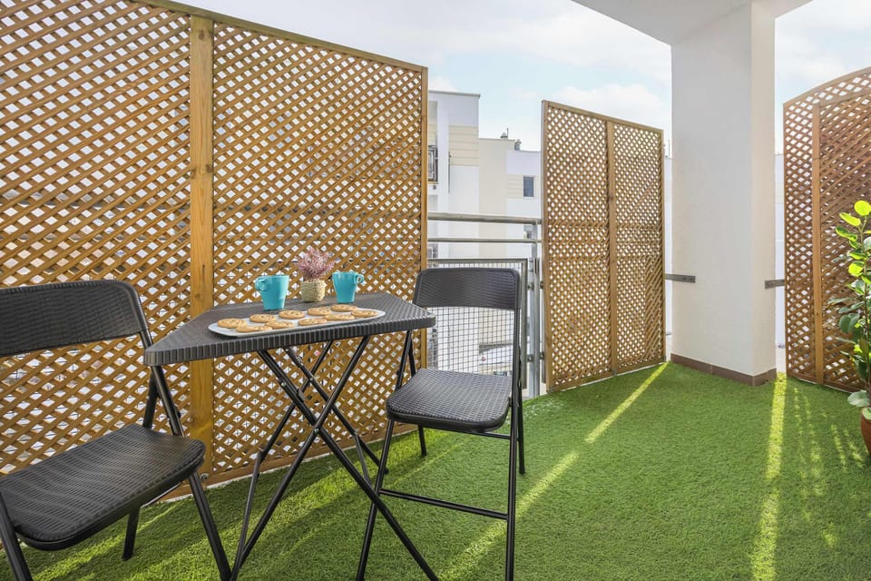 A cozy private balcony with green artificial grass and wooden privacy panels. It features a small table and chairs, perfect for relaxing outdoors.
