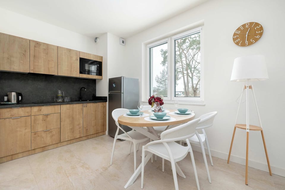 A functional kitchenette and dining area include a round wooden table with four modern white chairs and stylish wooden cabinetry.