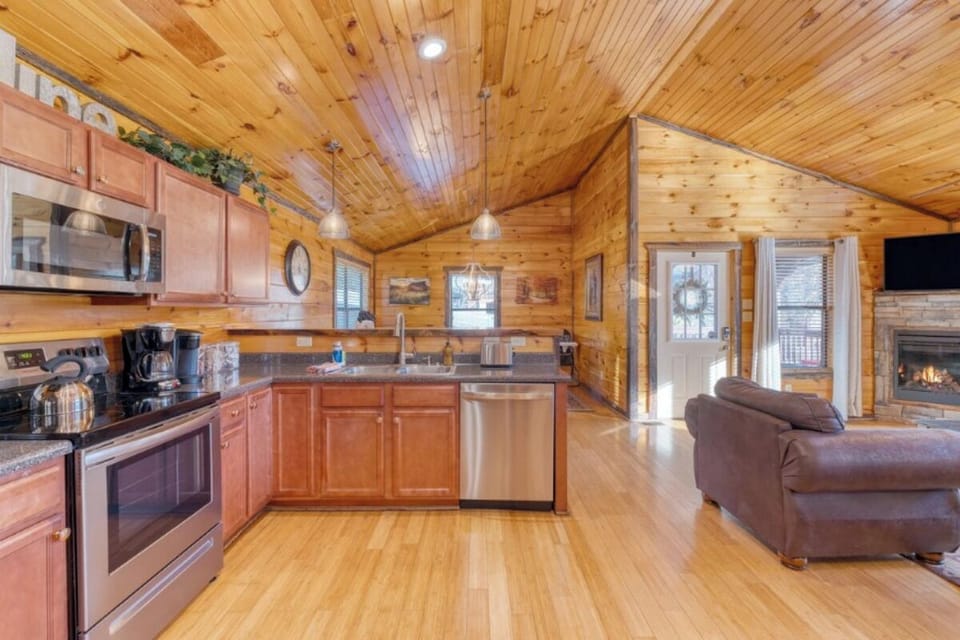 Your cozy cabin retreat features a fully equipped kitchen and comfortable living space with warm wood details and a stone fireplace.