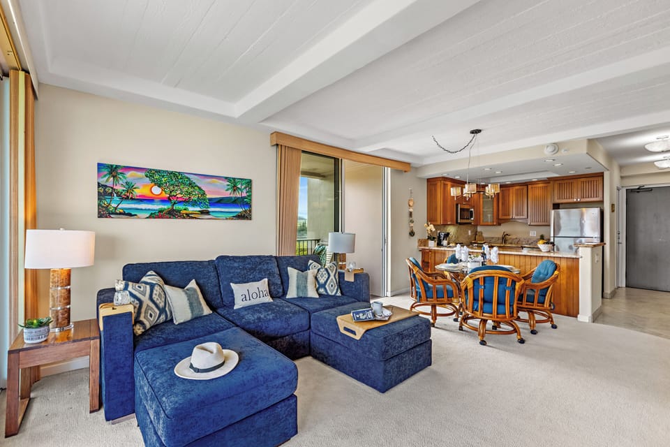 Relax in your tropical-themed living space with plush seating and a fully equipped kitchen, all under soaring white beam ceilings.