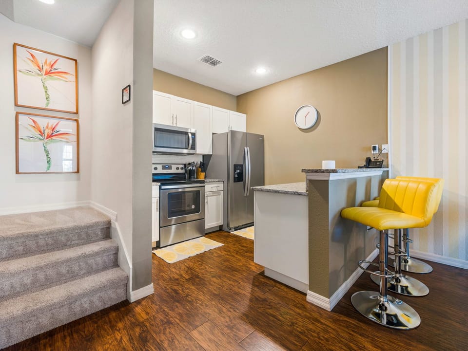 Modern kitchen with stainless steel appliances and a breakfast bar featuring yellow stools.
