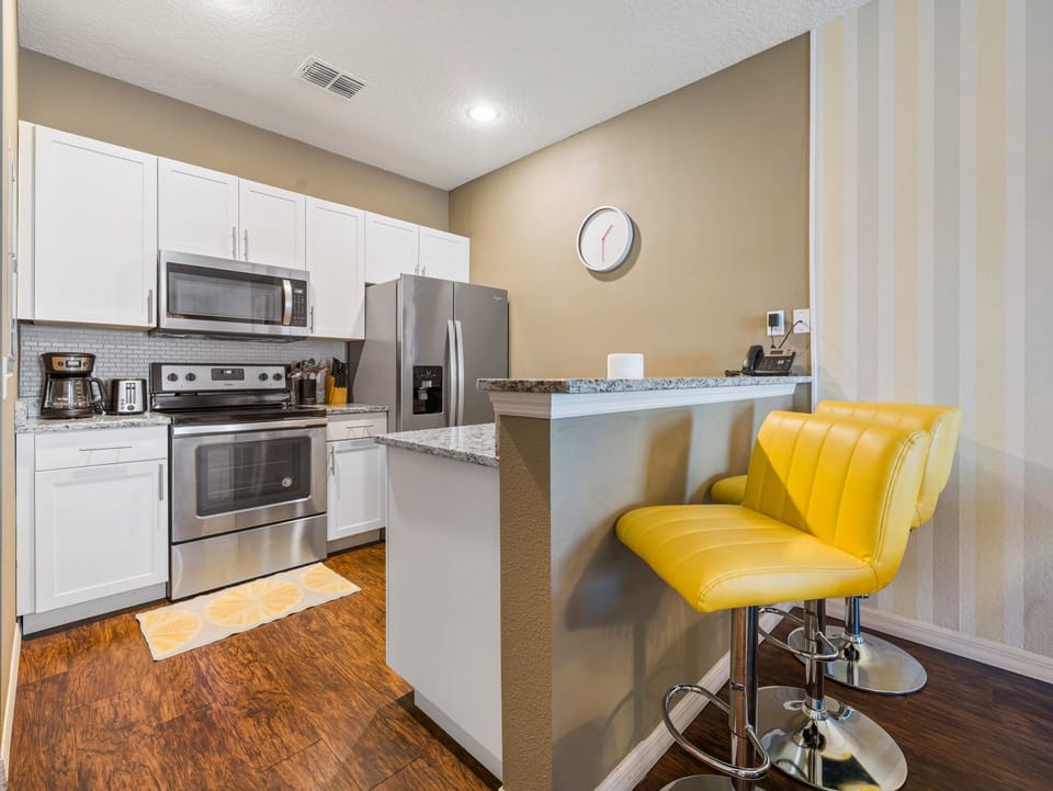 Modern kitchen with stainless steel appliances and a breakfast bar featuring yellow stools.