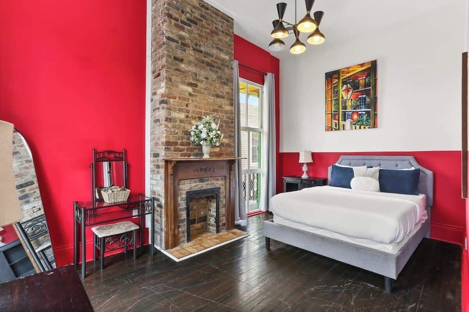 Stylish bedroom with a queen bed, exposed brick fireplace, and bold New Orleans–inspired design. High ceilings, natural light, and thoughtful touches create a comfortable, inviting retreat.