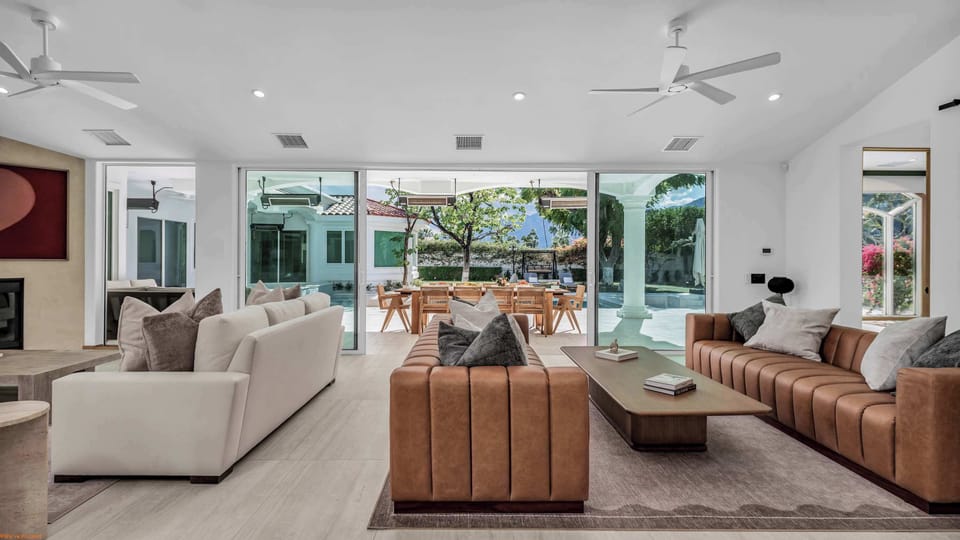Bright great room with leather channel sofas, floor-to-ceiling sliding glass walls opening directly to the pool patio and mountain views