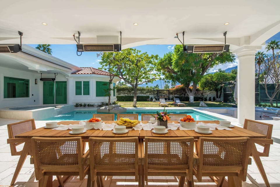 Bright covered outdoor dining for eight, pool and spa beyond, overhead heaters, and mountain views — breakfast alfresco every morning