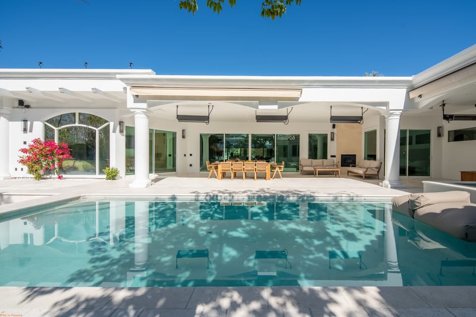 Bright resort-style pool with colonnaded covered patio, outdoor dining, lounge seating, and outdoor fireplace — your own Mediterranean escape
