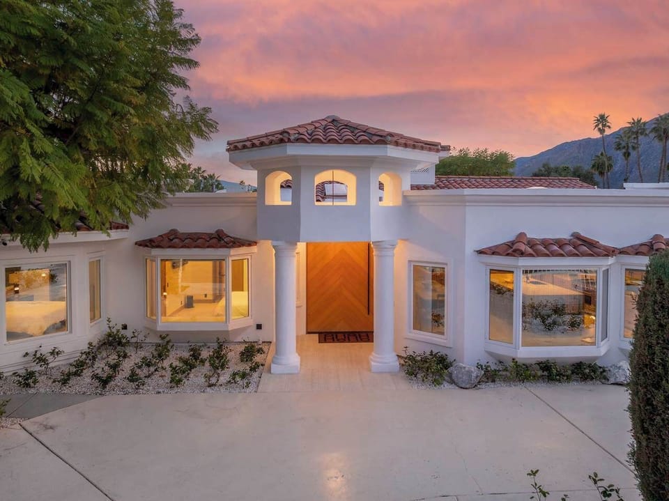 Twilight exterior — Mediterranean facade with terracotta tile roof, grand columned entry, herringbone pivot door, and mountain backdrop