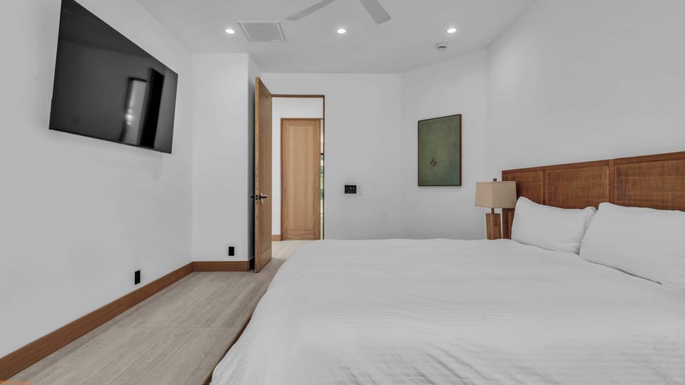 Bright bedroom with cane-panel headboard, wall-mounted TV, and ceiling fan — clean, calm, and resort-ready
