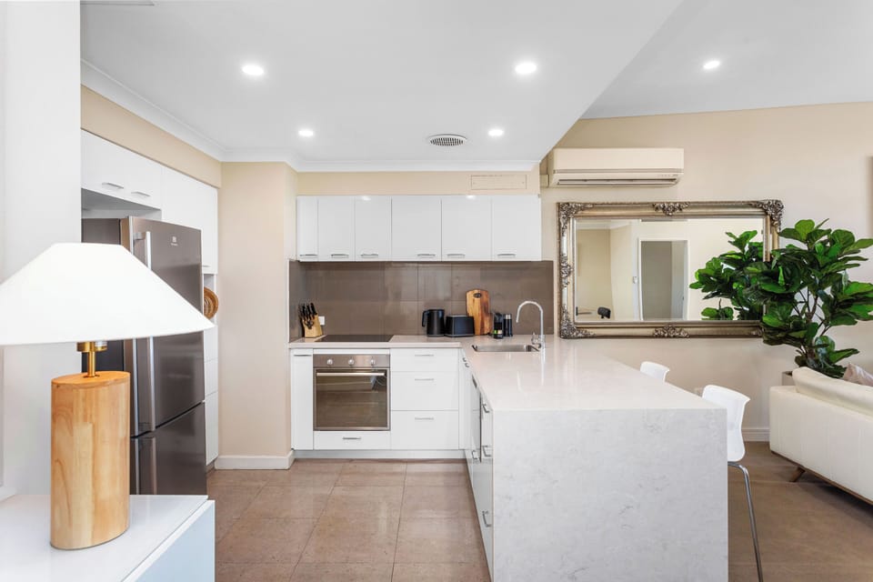 A bright, open-plan sanctuary featuring a designer kitchen with stone waterfall counters and floor-to-ceiling windows that reveal stunning, lush treetop views.