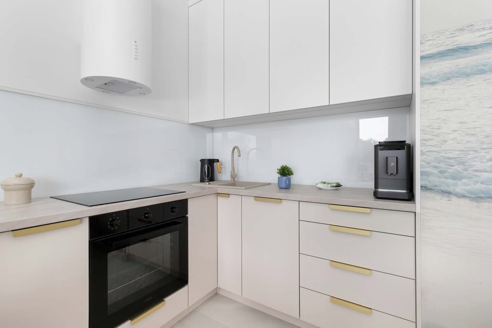 The kitchen corner features a clean, white backsplash and modern appliances, including a black oven. A tall window nearby ensures plenty of ventilation and light while cooking.