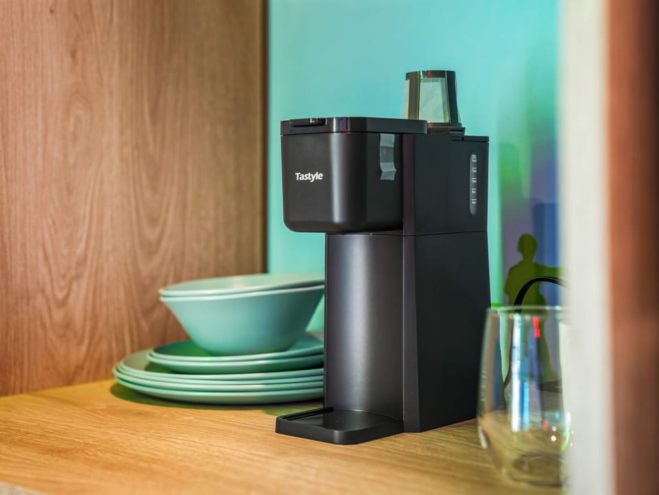 Modern coffee maker next to stacked turquoise dishes on a wooden countertop