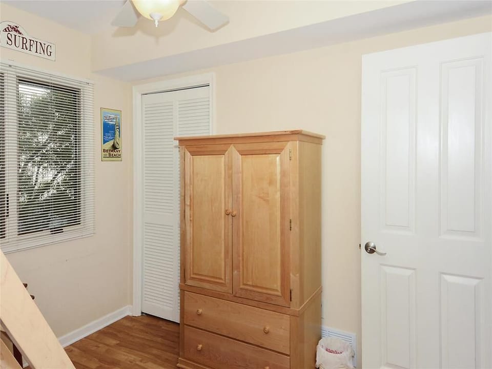 The bunk room includes a classic wooden wardrobe and a window with natural light filtering in, evoking a serene beach atmosphere.