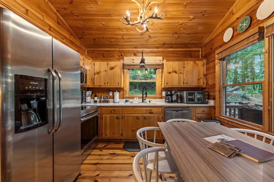 Rustic cabin kitchen with stainless appliances, coffee bar, and forest views.