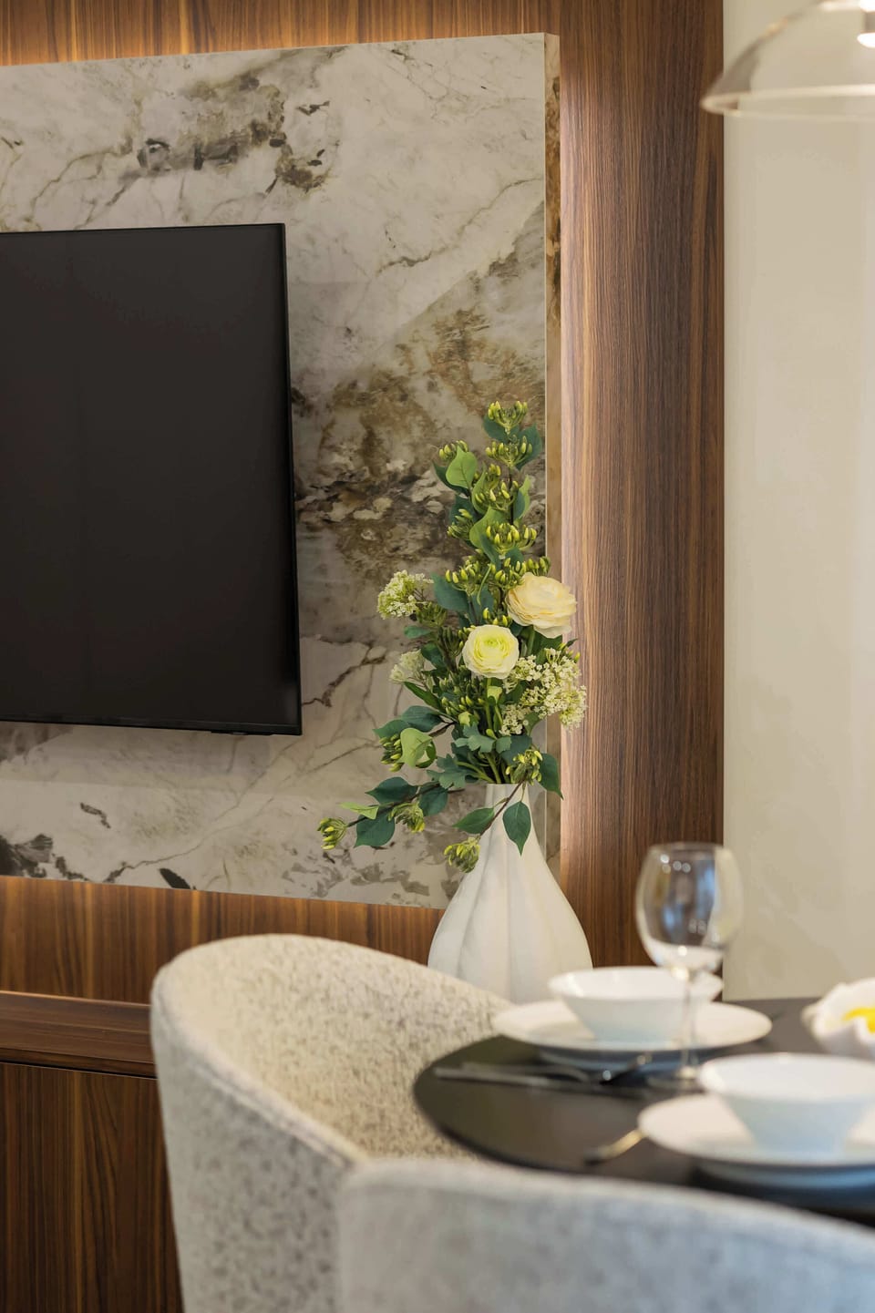 Close-up of a dining table with elegant tableware.  In the background, there is a flat-screen television on the wall.