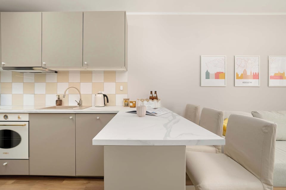 A modern open kitchenette with beigie cabinets and a white island countertop. Minimal decor and soft lighting give the space a clean, contemporary feel.