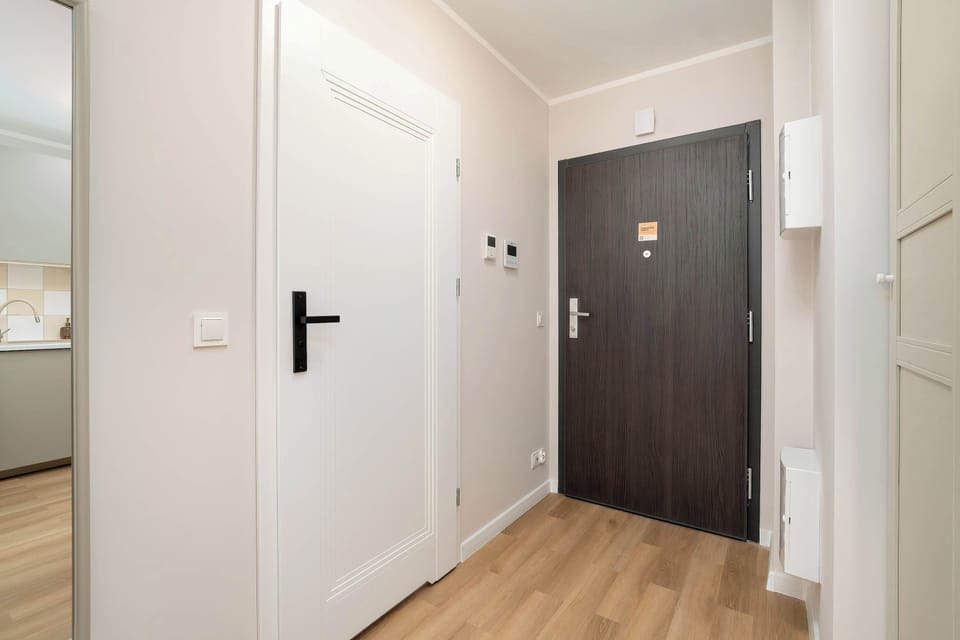 A hallway with light wood floors and dark entry doors. The space looks freshly finished and uncluttered.