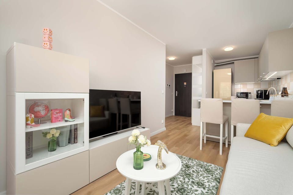 A wide view of the living and dining area with a white coffee table and decorative items on top. The kitchen is visible in the background, creating an open-plan layout.