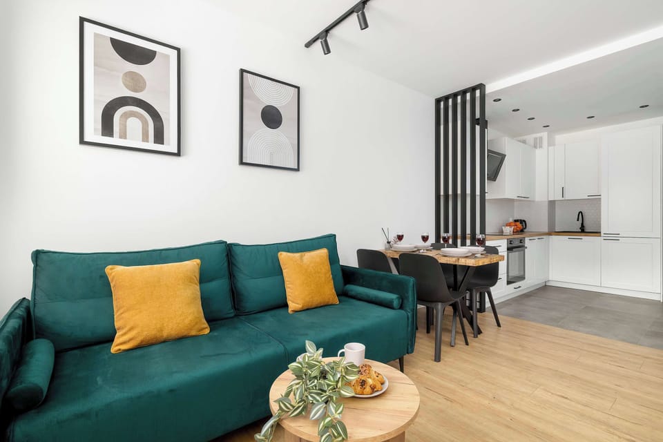 A wide-angle view of the living room showing the vibrant green sofa as a focal point against white walls. The space is decorated with abstract circular art pieces that tie the color scheme together.