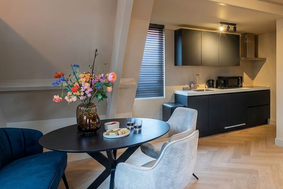 Stylish dining area with round table, flowers and seating, connected to a modern kitchen with dark cabinets, creating a warm and inviting space.