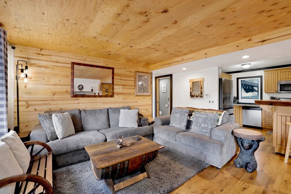 Cozy mountain living room with a stone fireplace, comfy seating, and smart TV—perfect for relaxing evenings, movie nights, and warm cabin vibes after outdoor adventures.