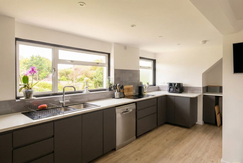 The kitchen provides worktop space along two walls, with a dishwasher and a sink positioned beneath a wide window overlooking the garden.