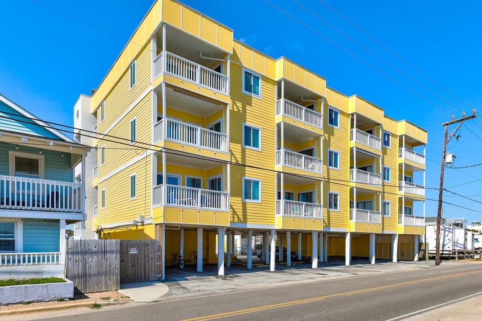 Bright yellow beachside building with multiple balconies offers coastal charm and convenient street access.